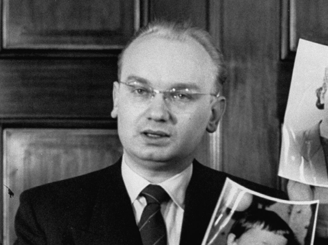 KGB agent Nikolai Khokhlov, who defected from the Soviet Union in 1954, holds up photos of his wife and son.