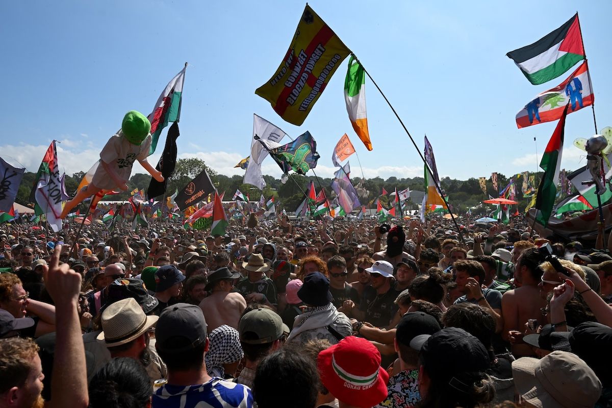 Flags raised above the crowd as Kneecap performs at Glastonbury Festival on June 28, 2025.