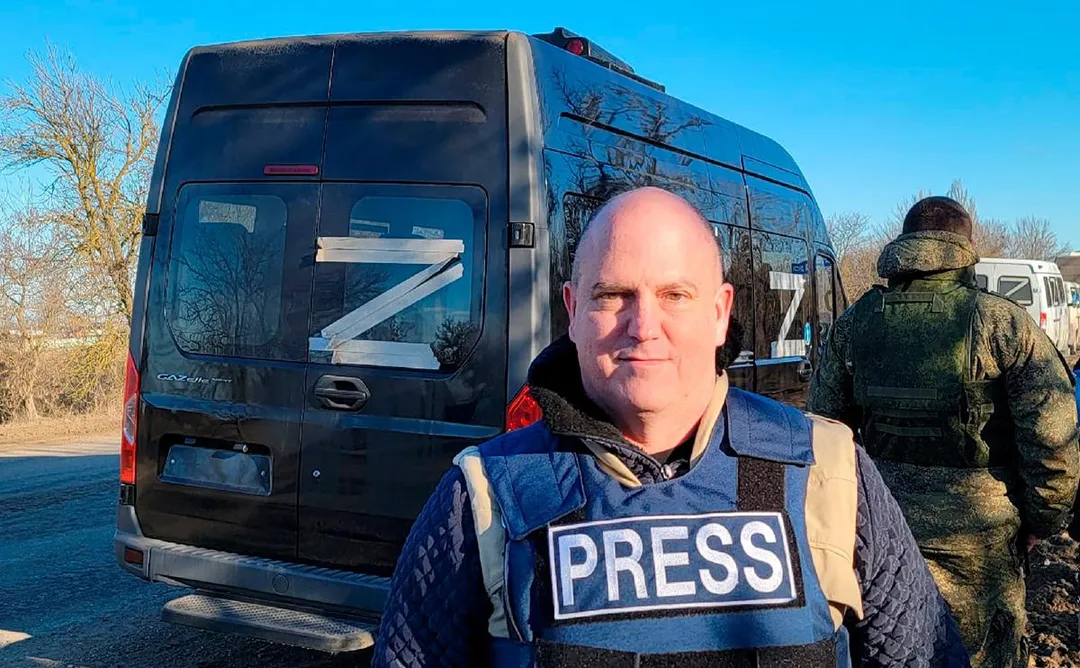 John Mark Dougan wearing a bulletproof press vest in front of a van bearing the taped-on Russian pro-war “Z” symbol